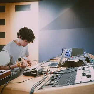 Músico tocando una guitarra eléctrica junto a una mesa de mezclas